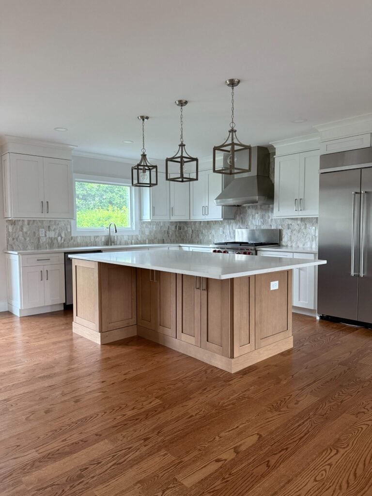 Modern kitchen with wood floors, a large central island, white cabinets, stainless steel appliances, and three pendant lights hanging above the island.