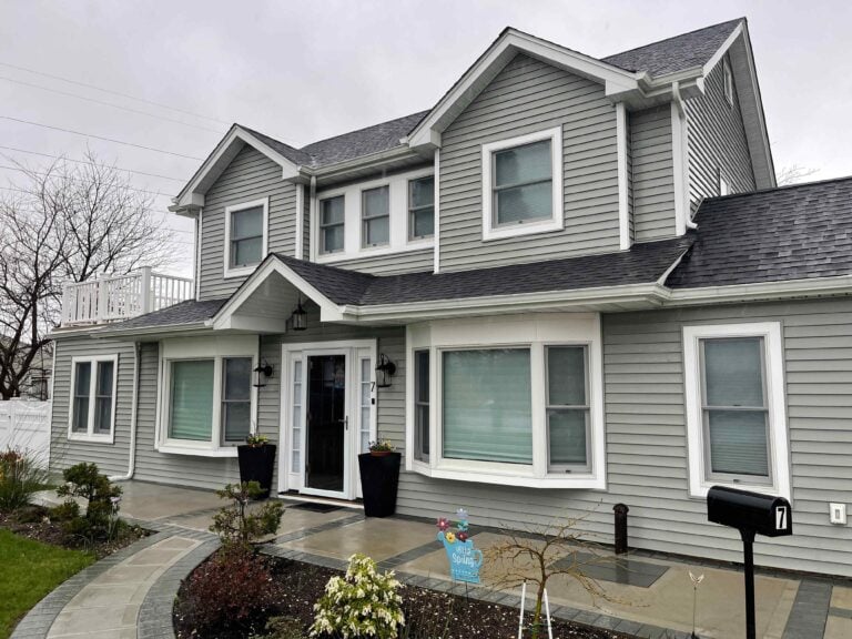 Two-story gray house with white trim, multiple windows, a black front door, a landscaped yard, and a black mailbox in front.