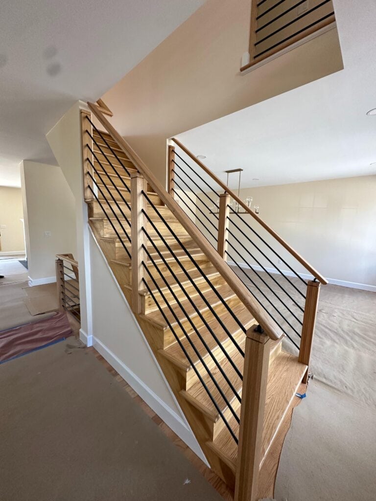 Wooden staircase with metal horizontal railings in a modern, unfinished interior space with carpet and bare floors.