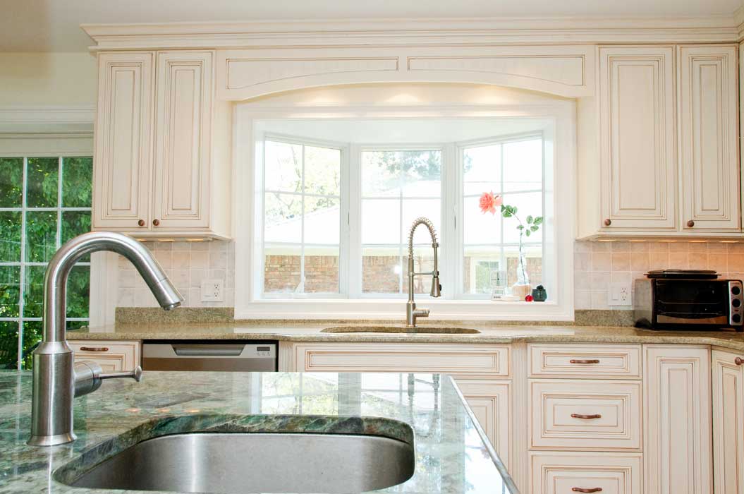 Modern kitchen with white cabinets, granite countertops, a large window above the sink, and a stainless steel faucet on a central island.
